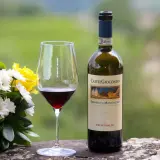 Un bicchiere di vino rosso accanto a una bottiglia di Brunello di Montalcino, con un bouquet di fiori bianchi e gialli.