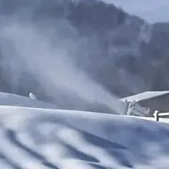 Neve artificiale sul Monte Penice, con un cannone spara-neve in azione e un rifugio sullo sfondo.