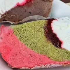 Un pezzo duro gelato a strati: rosa, verde pistacchio e bianco con striature rosse. Un altro pezzo di gelato al cioccolato e bianco è sullo sfondo.