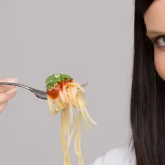 Donna con forchettata di spaghetti al pomodoro, un piatto che sembra quasi un'opera d'arte con i suoi formati di pasta strani e invitanti.