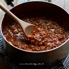 Un pentolone pieno di ragù, pronto per condire gli spaghetti. Un cucchiaio di legno mescola la salsa.