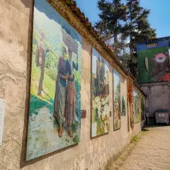 Opere d'arte lungo un muro a Gravellona Lomellina, con dipinti che raffigurano scene di vita rurale. Un'installazione artistica colorata completa il panorama.