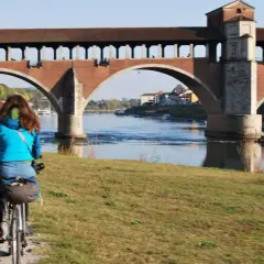 Ciclista sulla ciclabile Milano Pavia, con il Ponte Coperto di Pavia sullo sfondo.