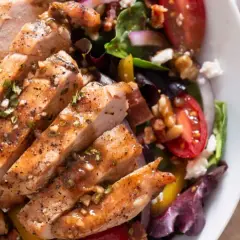 Deliziosa insalata estiva gourmet con pollo grigliato, pomodorini, noci e formaggio feta. Perfetta per un pasto leggero e saporito.