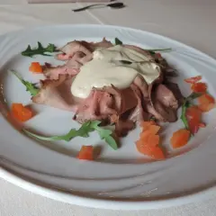 Vitello tonnato, un classico con origini piemontesi, servito su un piatto bianco con pomodorini e rucola.