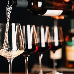 Versando vino bianco in un calice, con altri calici pieni di un intenso rosso rubino sullo sfondo.