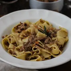 Pappardelle con ragù di carne, un classico dei primi piatti di carne, guarnite con rosmarino.