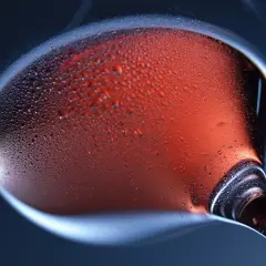Un bicchiere di vino rosato, con goccioline di condensa sulla superficie, evoca la freschezza e l'eleganza della vinificazione in rosato.