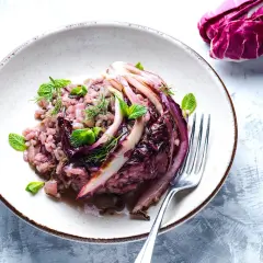 Un cremoso risotto al radicchio, guarnito con foglie di menta fresca e aneto, pronto per essere gustato.