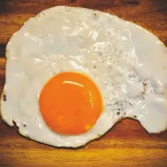 Un uovo in cereghin, cotto alla perfezione, con un tuorlo arancione brillante su un tagliere di legno scuro.