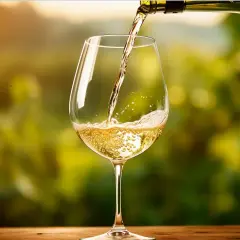 Versando un vino bianco dorato, un Trebbiano d'Abruzzo, in un calice su un tavolo di legno, con uno sfondo sfocato di vigneti al tramonto.