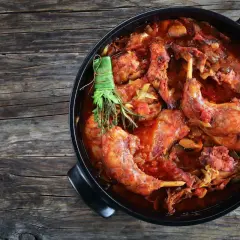 Un saporito coniglio al vino rosso, cotto lentamente con erbe aromatiche, in una casseruola nera su un tavolo di legno rustico.
