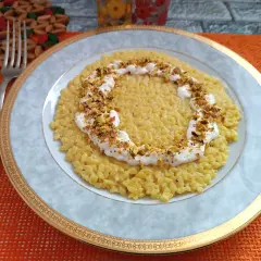 Un cremoso risotto con robiola e zafferano, guarnito con pistacchi tritati, pronto per essere gustato.