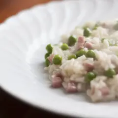 Un cremoso riso con piselli e cubetti di prosciutto, servito su un piatto bianco con un bordo ondulato.
