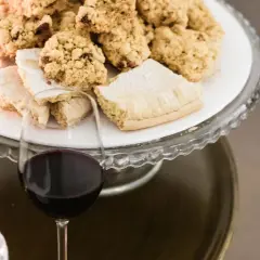 A glass of red wine sits next to a cake stand filled with cookies and pastries.