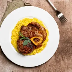 Ossobuco con risotto alla milanese, un classico dei piatti tipici Lombardia, guarnito con rosmarino e salvia.