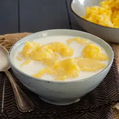 Una ciotola di polenta e latte, un piatto confortante. Accanto, una bottiglia di latte e un cucchiaio d'argento.