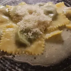 Ravioli italiani ripieni, conditi con una salsa cremosa e spolverati di parmigiano grattugiato, serviti in un piatto scuro.