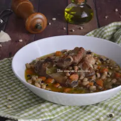 Una ciotola di zuppa dei morti con fagioli, costine di maiale e carote, servita su una tovaglia a quadri verdi.