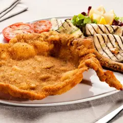 Cotoletta alla milanese dorata e croccante, servita con pomodori grigliati, melanzane e un'insalata fresca.