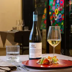 Un bicchiere di vino bianco Catarratto, con le sue caratteristiche freschezza e note agrumate, accompagna un piatto gourmet.