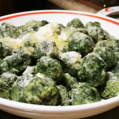 Malfatti ricetta originale: gnocchetti verdi fatti in casa, conditi con burro fuso e parmigiano grattugiato, serviti in una ciotola bianca con bordo rosso.