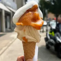 Cono con gelato artigianale, bianco e arancione, con un tocco di gelato contadino. Perfetto per una passeggiata estiva.