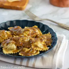 Piatto di agnolotti al brasato, conditi con un sugo ricco e saporito, serviti su un piatto scuro.