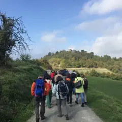 Gruppo di escursionisti sul sentiero delle fontane, con colline boscose e un borgo in cima.