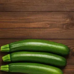 Tre zucchine fresche su un tavolo di legno scuro, pronte per fantastiche ricette con zucchine.