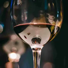 Un bicchiere di vino rosso riflette luci sfocate. Immagina tre bicchieri pronti per una degustazione serale.