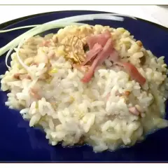 Un cremoso risotto pere e speck, guarnito con noci e fili di porro.
