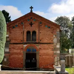 Chiesa in mattoni rossi con croce in cima, circondata da alberi verdi. Un luogo tranquillo, forse a Voghera dove si trova.