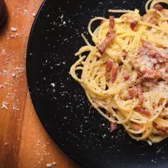 Spaghetti alla carbonara, un piatto che evoca la sua origine romana, con guanciale croccante e pecorino.