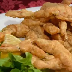 Un piatto di croccanti rane fritte, servite con spicchi di limone e foglie di lattuga fresca.