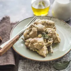 Piatto di coniglio al latte, tenero e saporito, guarnito con rosmarino. Accanto, olio e latte in caraffa.