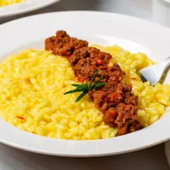 Risotto giallo cremoso con ragù di salsiccia e stracchino, guarnito con rosmarino.