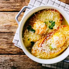 Zuppa alla pavese fumante, con pane tostato, uova e abbondante parmigiano grattugiato, servita in una ciotola bianca su un tavolo di legno rustico.