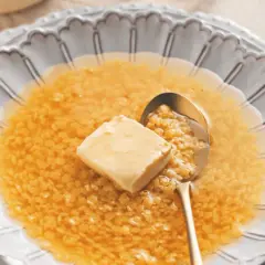 Minestrina in brodo con dado, un comfort food che scalda il cuore. Un cucchiaio d'oro raccoglie la pasta minuta e un cubetto di burro si scioglie nel brodo caldo.