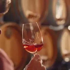 Uomo degusta vino rosso in cantina, tra botti di legno. Un assaggio del vero super tuscany.