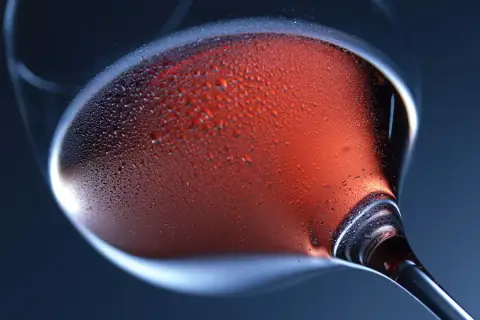 Un bicchiere di vino rosato, con goccioline di condensa sulla superficie, evoca la freschezza e l'eleganza della vinificazione in rosato.