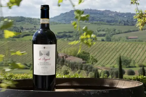 Bottiglia di Vino Nobile di Montepulciano in primo piano, con vigneti e colline toscane sullo sfondo.