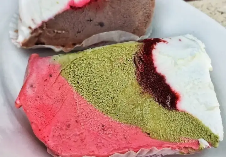 Un pezzo duro gelato a strati: rosa, verde pistacchio e bianco con striature rosse. Un altro pezzo di gelato al cioccolato e bianco è sullo sfondo.