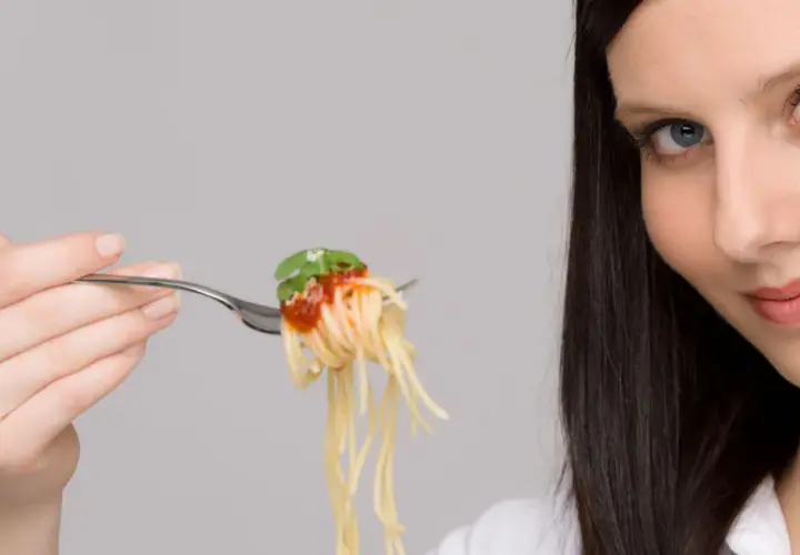 Donna con forchettata di spaghetti al pomodoro, un piatto che sembra quasi un'opera d'arte con i suoi formati di pasta strani e invitanti.