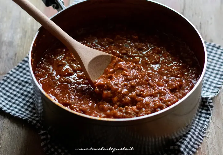 Un pentolone pieno di ragù, pronto per condire gli spaghetti. Un cucchiaio di legno mescola la salsa.