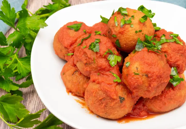 Pallotte cacio e ova, gustose polpette in salsa di pomodoro, guarnite con prezzemolo fresco.