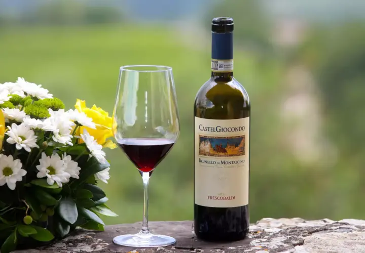 Un bicchiere di vino rosso accanto a una bottiglia di Brunello di Montalcino, con un bouquet di fiori bianchi e gialli.