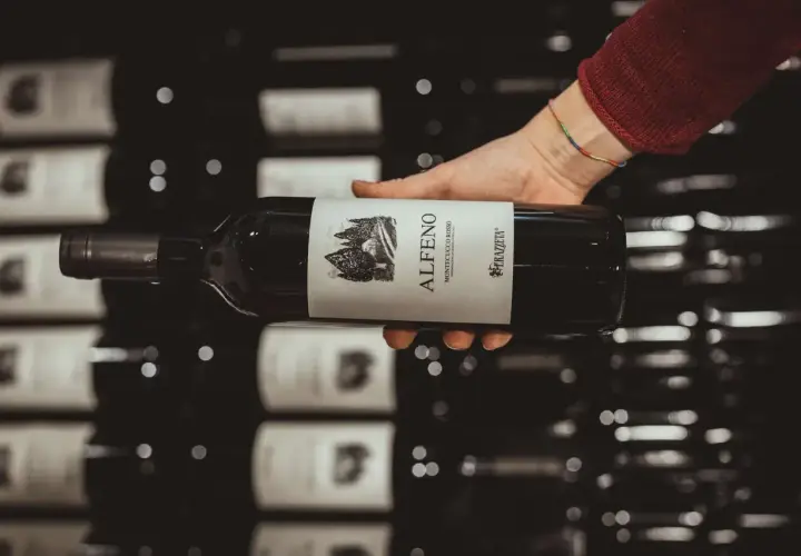 Mano che tiene una bottiglia di vino rosso "Alfero Montecucco Rosso". Il Cabernet Sauvignon, di cui questa regione è originaria, è un vitigno internazionale.