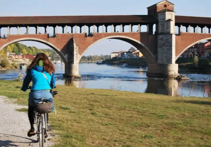 Ciclista sulla ciclabile Milano Pavia, con il Ponte Coperto di Pavia sullo sfondo.