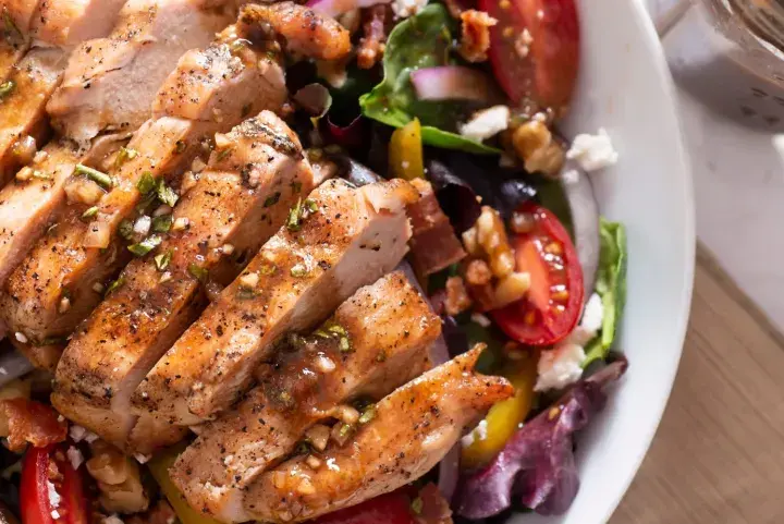 Deliziosa insalata estiva gourmet con pollo grigliato, pomodorini, noci e formaggio feta. Perfetta per un pasto leggero e saporito.